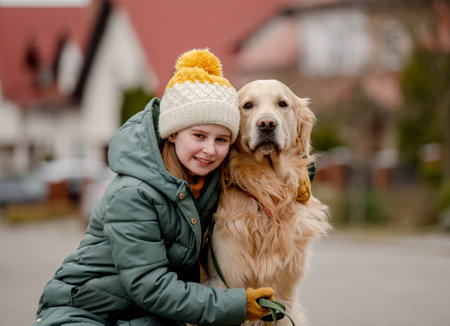 Preteen child girl hugging golden retriever dog at autumn city street wearing hat and warm jacket. Pretty kid with purebred pet doggy labrador outdoorsの写真素材