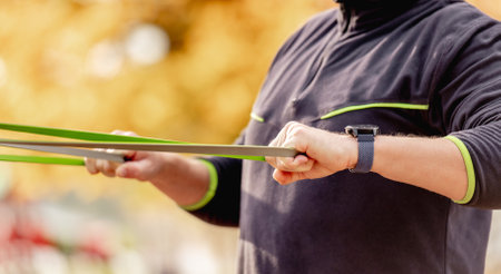 Strong man guy training with elastic rubber band at the stadium outdoors. Adult male person during workout for arms and chest with additional sport equipmant. Sportsman exercising outsideの写真素材