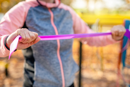 Girl doing arms ezxercises with elastic rubber band at autumn time outdoors. Young woman during hands and cheast training workoutの写真素材