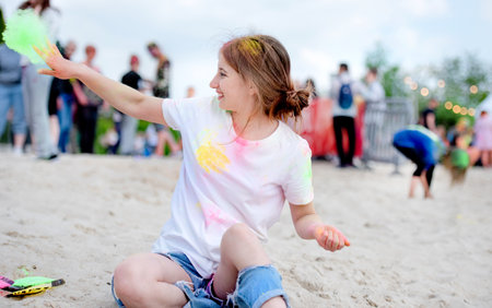 Pretty girl in indian traditional Holi festival sitting at beach sand with colorful powder and having fun. Female teenager enjoying positive holidayの写真素材