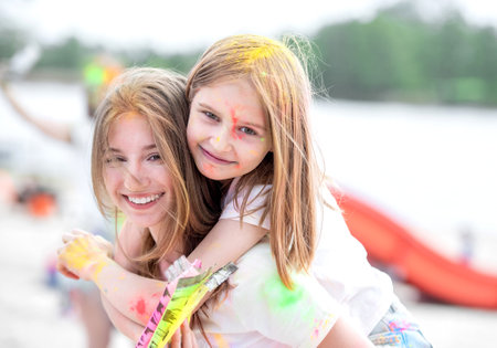 Pretty girls sisters in indian Holi festival with colorful powder smiling and having fun. Female teenager and preteen child friends enjoying holidayの写真素材