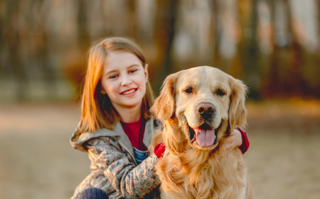 Preteen girl with golden retriever dog sitting in park in beautiful spring autumn day.の写真素材