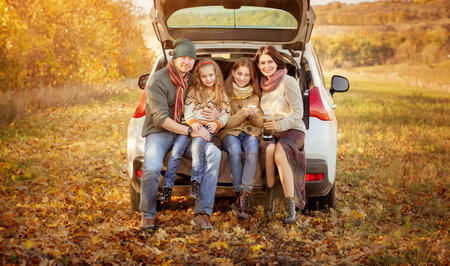 Happy family sitting in car trunk on autumn backgroundの写真素材