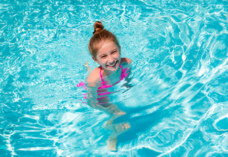 Portrait of lovely little teenage girl ressting on the edge of swimming pool and squinting her eyes because of the bright sunの写真素材