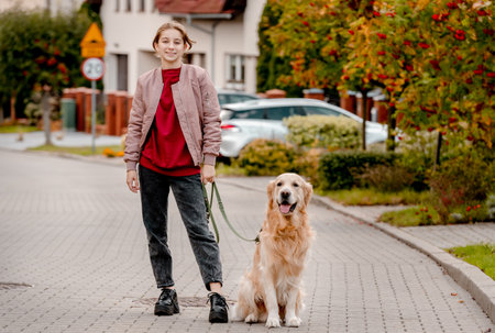 Preteen teen girl in pink jacket with golden retriever dog on lace looking at camera. Female child kid with a purebred labrador doggy petの写真素材