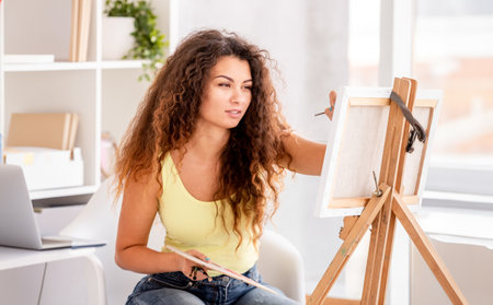 Beautiful girl painting picture on easel in light roomの写真素材