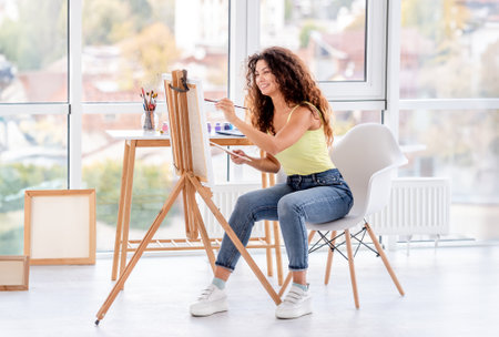 Smiling artist painting on easel in workshopの写真素材