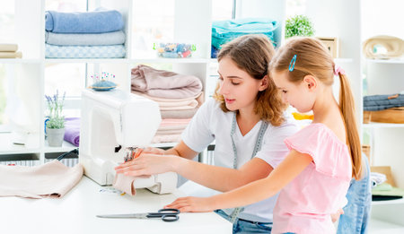 Little girl is taught to sew by teacher at classの写真素材
