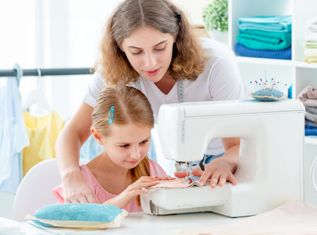 Little girl is taught to sew by teacher at classの写真素材
