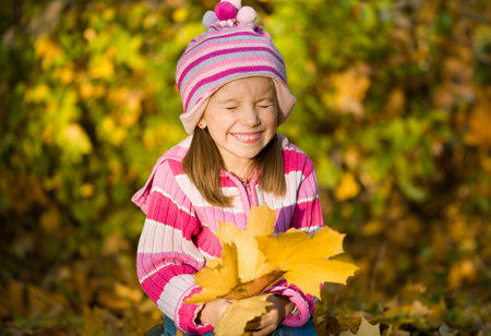 little girl squinting against autumn leavesの写真素材