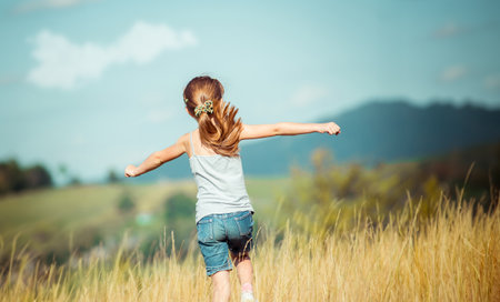 little girl runs through a beautiful meadow in the mountains. back viewの写真素材