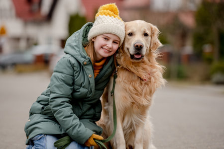 Preteen child girl hugging golden retriever dog at autumn city street wearing hat and warm jacket. Pretty kid with purebred pet doggy labrador outdoorsの写真素材