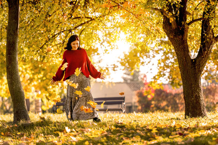 Pretty girl posing in autumn park with yellow leaves. Attractive young woman wearing cozy beautiful dress in fall season with golden foliage at natureの写真素材