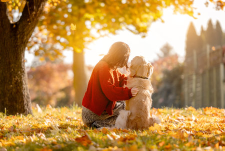 Beautiful girl hugging golden retriever dog in autumn park sitting in yellow leaves and looking at sun. Pretty young woman with purebred doggy labrador at fall season at natureの写真素材