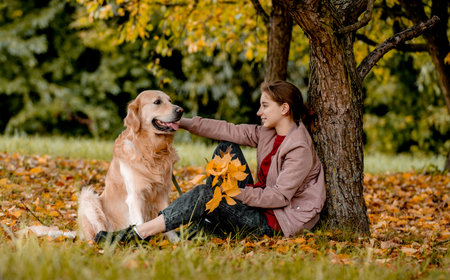 Preteen girl with golden retriever dog sitting in park in beautiful spring autumn day. Adorable female child kid and doggy pet outdoors and smiling portraitの写真素材