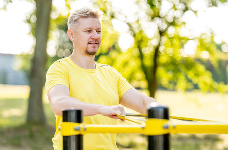 Man excercising with elastic rubber band outdoors making arm workout. Guy making fitness with sport equipment and training stretghtの写真素材