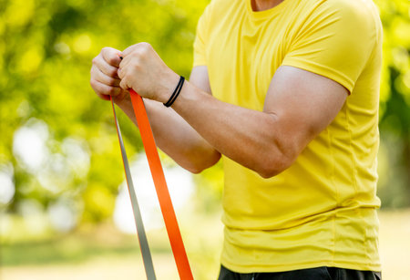 Man excercising with elastic rubber band outdoors making arm workout. Guy making fitness with sport equipment and training stretghtの写真素材