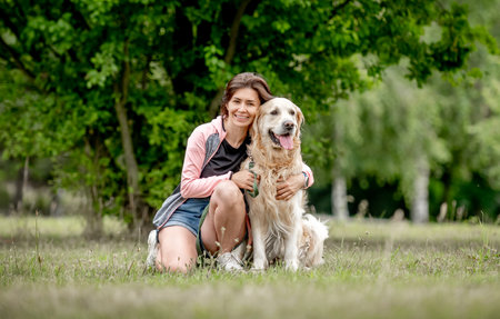 Pretty girl with golden retriever dog sitting at nature. Beautiful young woman hugging purebred pet doggy labrador in park at summerの写真素材