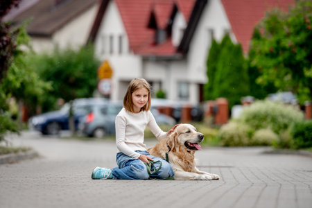 Preteen girl with golden retriever dog sitting at city street and looking back. Pretty child kid with purebred pet doggy outdoorsの写真素材