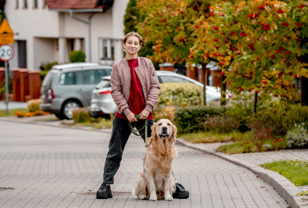 Preteen teen girl in pink jacket with golden retriever dog on lace looking at camera. Female child kid with a purebred labrador doggy petの写真素材