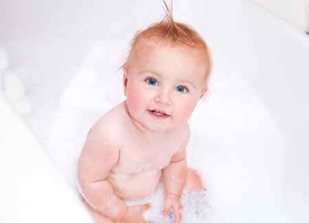 pretty smiling baby girl is taking a bath with a foamの写真素材