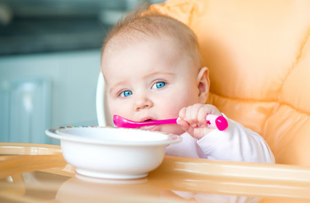 smiley baby girl is holding a spoon in her mouth and going to eatの写真素材