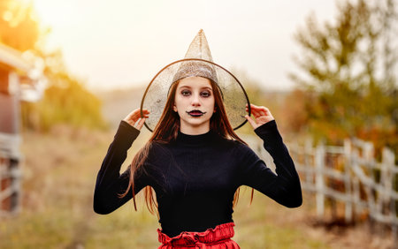 halloween portrait of teenage girl in witch hat smiling at camera on nature backgroundの写真素材