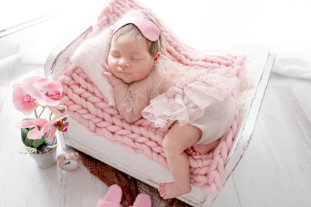 Adorable newborn baby girl sleeping in tiny bed on knitted blanket. Cute infant child kid in pink dress napping with orchid flower decorationの写真素材
