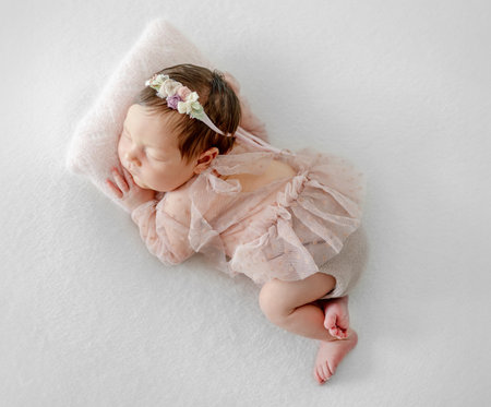 Adorable newborn baby girl sleeping on pillow. Cute infant child kid in pink dress and wreath napping lying on tummyの写真素材