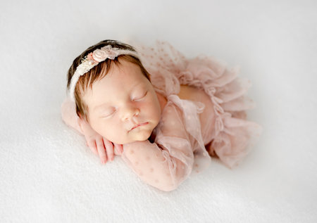 Adorable newborn baby girl sleeping on pillow. Cute infant child kid in pink dress and wreath napping lying on tummyの写真素材