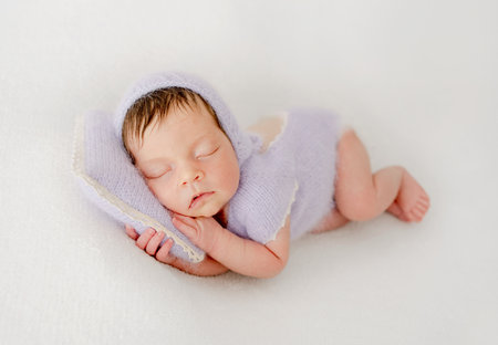 Adorable newborn baby girl sleeping on pillow. Cute infant child kid in knitted dress napping lying on tummyの写真素材