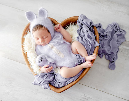 Adorable newborn baby girl in knitted dress and bunny hat sleeping in basket with rabbit toy. Cute infant child kid napping in heart shape bedの写真素材