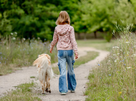 Preteen girl with golden retriever dog walking at nature. Cute child kid with purebred pet doggy labrador in park at summerの写真素材