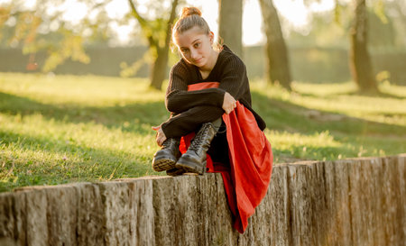 Beautiful teenager girl in red skirt sitting in park outdoors at nature. Pretty teen model in trendy clothes at streetの写真素材