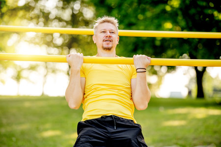 Man doing pull ups with horizontal bar outdoors in park for healthy wellbeing. Sportsman guy making strong workout for muscleの写真素材