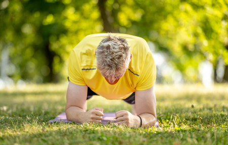 Man standing in plank position and practicing yoga outdoors at summer. Guy doing pilates workout for stretching muscles and abs stretghtの写真素材
