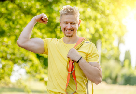 Man with elastic rubber band showing muscles outdoors after arm workout. Guy with sport equipment looking at camera and smilingの写真素材
