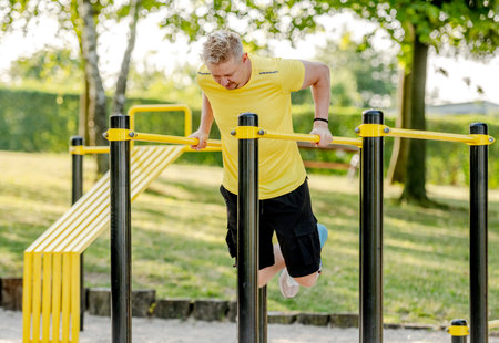 Man doing push ups with horizontal bar outdoors in park for healthy wellbeing. Sportsman guy making...