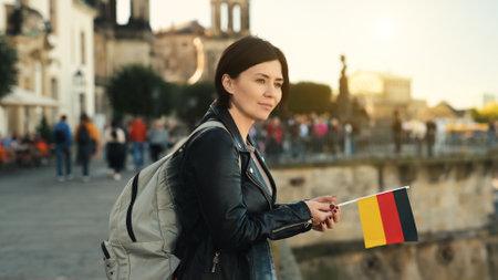 Young Woman Holds German Flag In Hand, With Blurred City Background In Autumnの写真素材