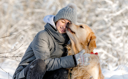 Teenage Girl And Golden Retriever Sit Together In Snow-Covered Forest During Winterの写真素材