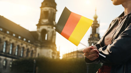 Young Woman Holds German Flag In Hand, With Blurred City Background In Autumnの写真素材