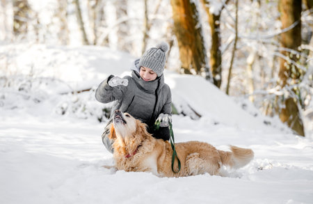 Teenage Girl Plays With Golden Retriever In Snowy Forest, Sitting With Dogの写真素材
