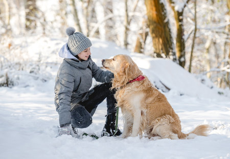 Teenage Girl And Golden Retriever Sit Together In Snow-Covered Forest During Winterの写真素材