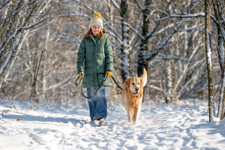Girl Walks With Golden Retriever In Winter Forest, Strolling With Dog Through Snow-Covered Woodsの写真素材