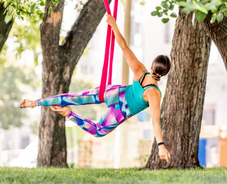 Beautiful girl during fly yoga in hammock at nature. Young sport woman doing aero fitness gymnastic stretching outdoorsの写真素材