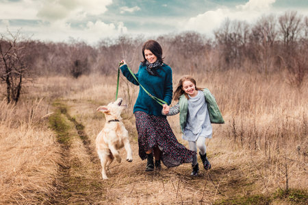 Playful dog walking with girl and woman outsideの写真素材