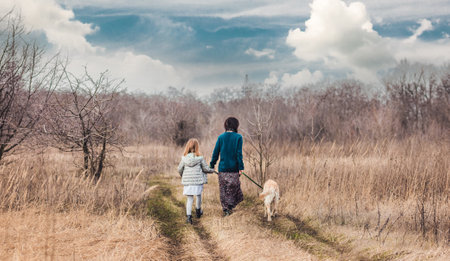 Mother and daughter walking dog along dirt roadの写真素材