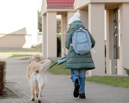 Girl With Golden Retriever Strolls Down Street In Early Spring, Viewed From Behindの写真素材