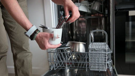 Young Woman Is Loading Spoons Into Dishwasher In Close-Up View