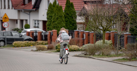 Girl Rides Bicycle Among Private Houses In Europe During Spring, View From Behindの写真素材